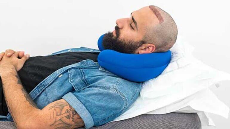 Person sleeping on their back with head elevated on a neck pillow after hair transplant.